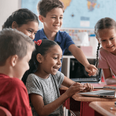 Group of young kids in a classroom collaborating in front of a laptop