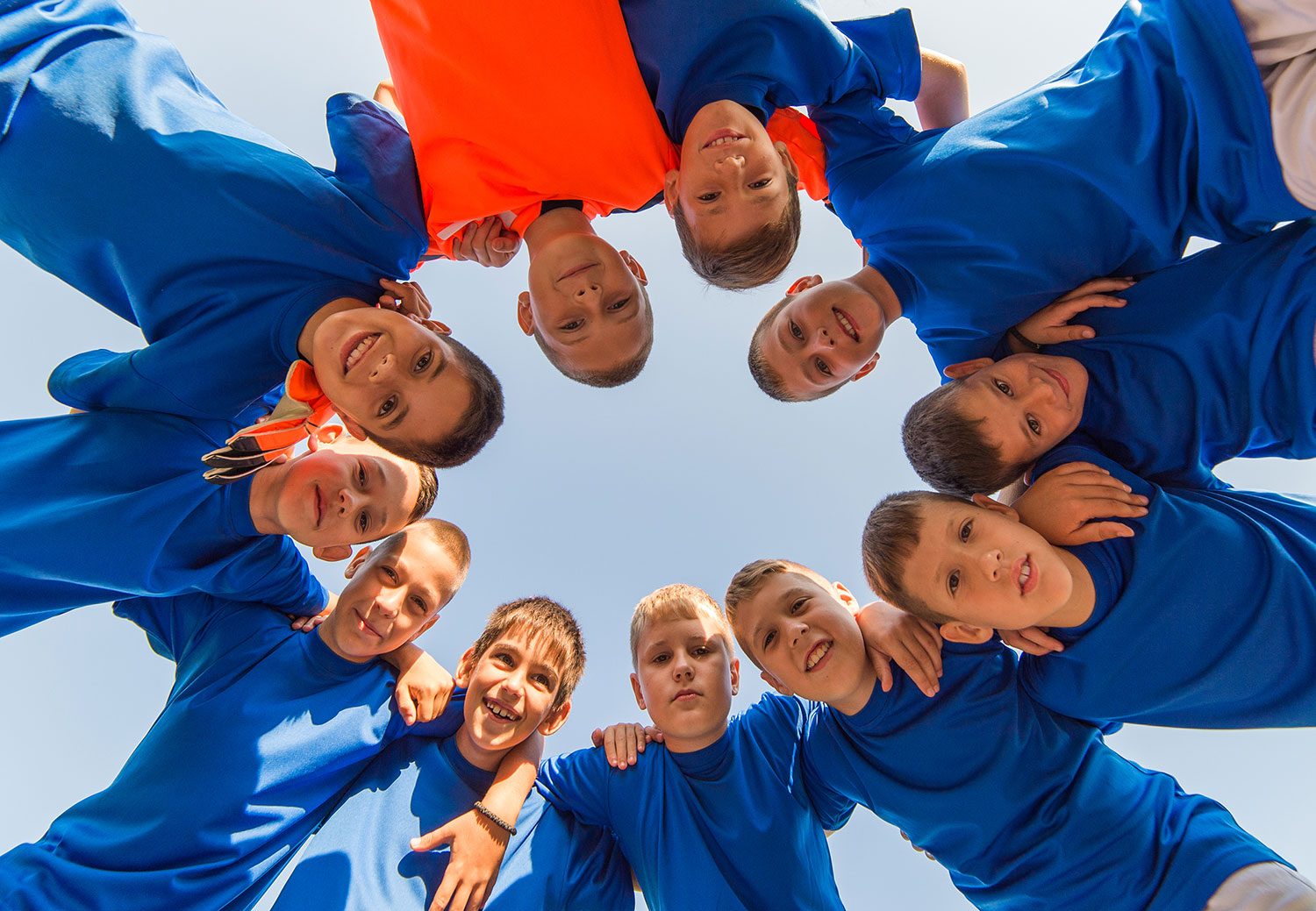 group of kids arms wrapped around each others shoulder forming a circle together looking down