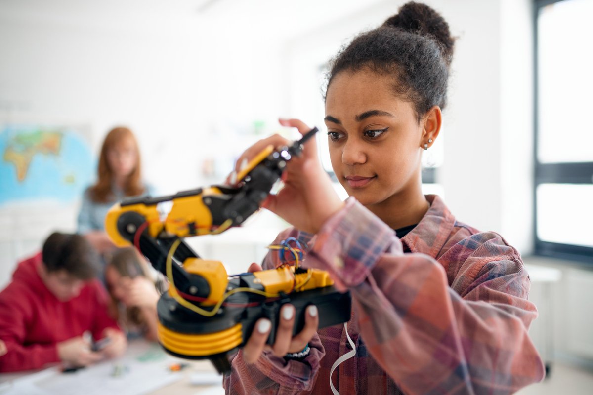 Teenage girl in classroom holding a robotic arm