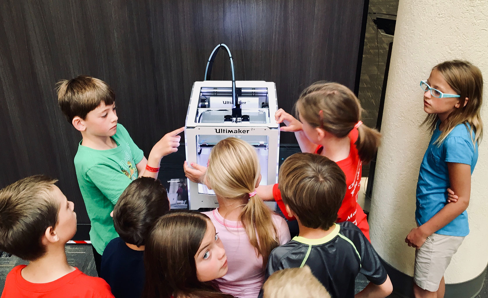 kids gathered around and interested at a 3d printer
