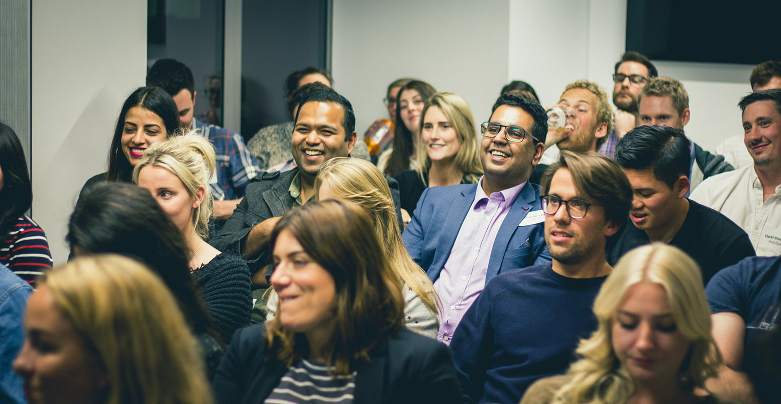 A group of business casual adults in an audience listening to a speaker