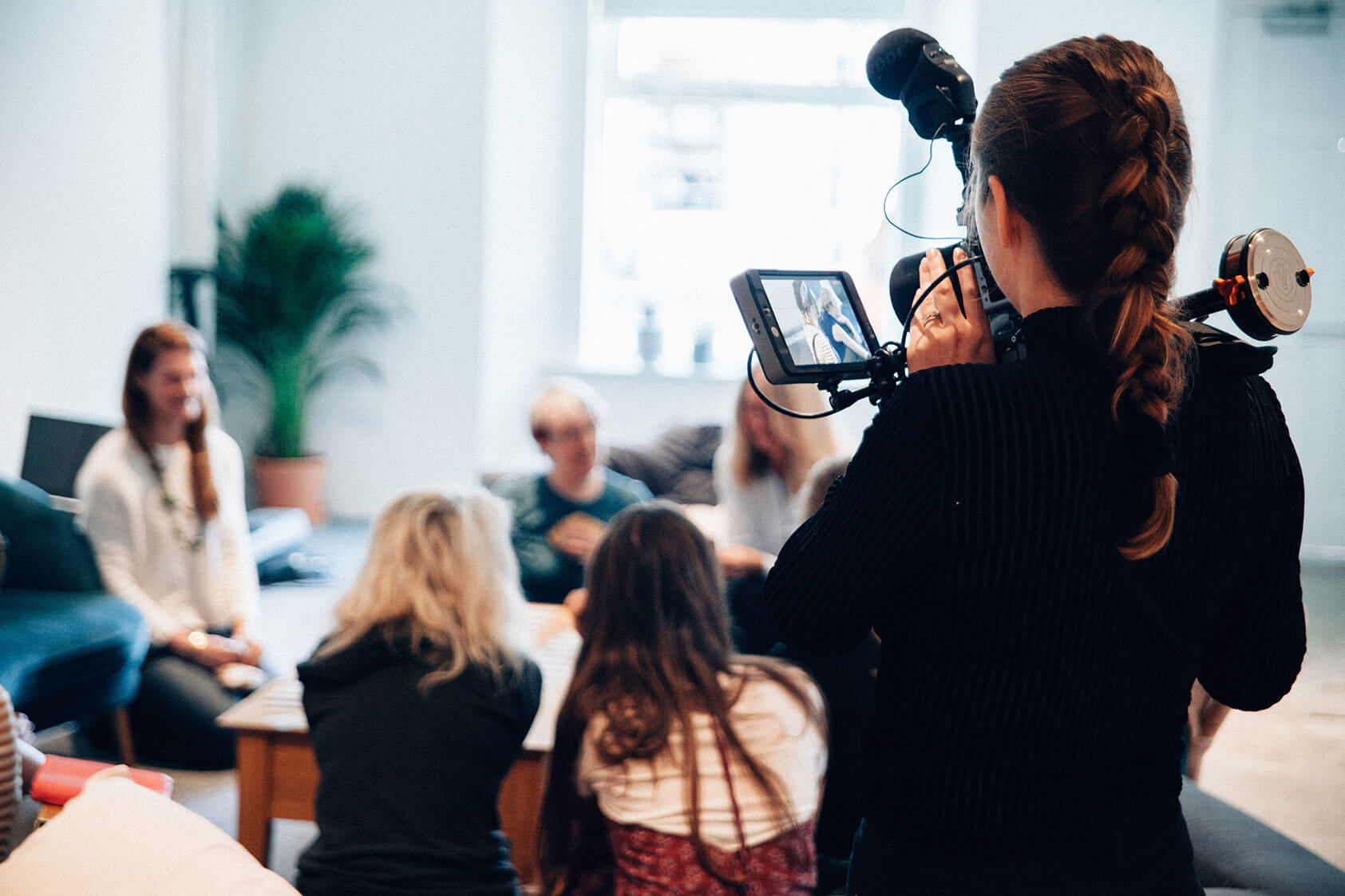 woman with camera filming a group of people in a school lounge