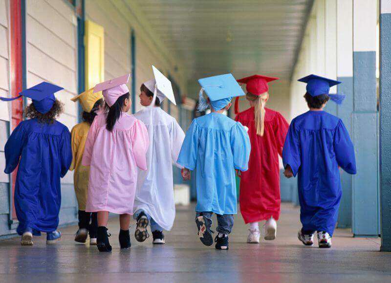 niños con togas de graduación caminando por el pasillo de una escuela exterior