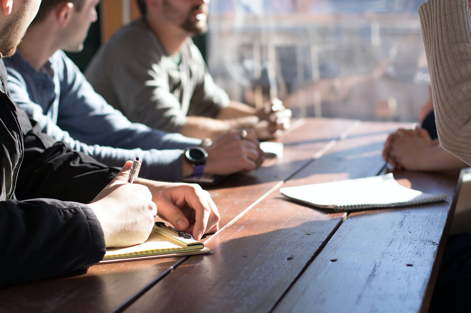 personas con mentalidad empresarial sentadas alrededor de una mesa debatiendo con papel y bolígrafo en la mano