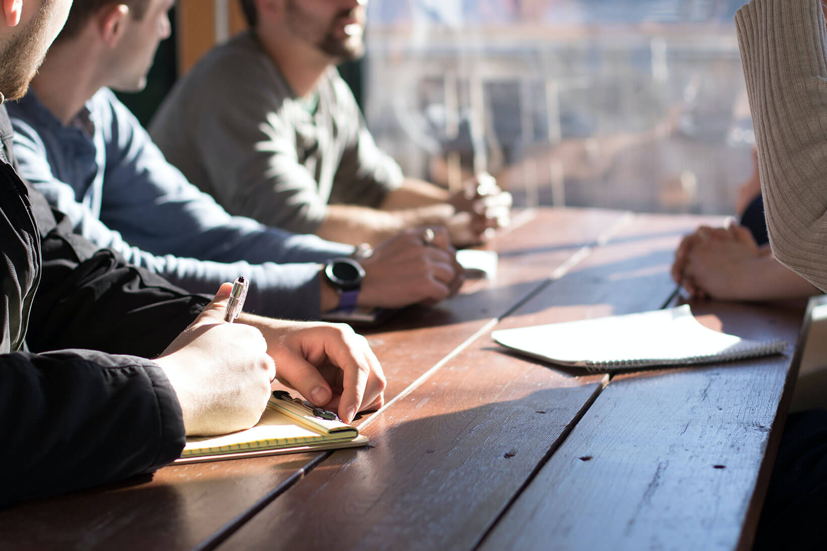 business minded individuals sitting around a table discussing with pen and paper at hand